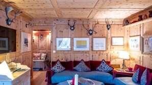 Un interior de cabaña acogedor, con techo de madera, un conjunto de sofás, una mesa de comedor y cuadros en las paredes.