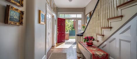 A hallway with a staircase, a red door, and a bench with a red tablecloth.