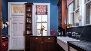 A kitchen with wooden cabinets, a white door, a window with a patterned valance, and a countertop with various items. - Victorian on Washington king bed near King St Hot Tub (Alexandria)