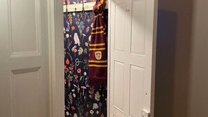 A hallway with a door leading to a room with a floral curtain and a maroon towel hanging on a hook. - Victorian on Washington king bed near King St Hot Tub (Alexandria)