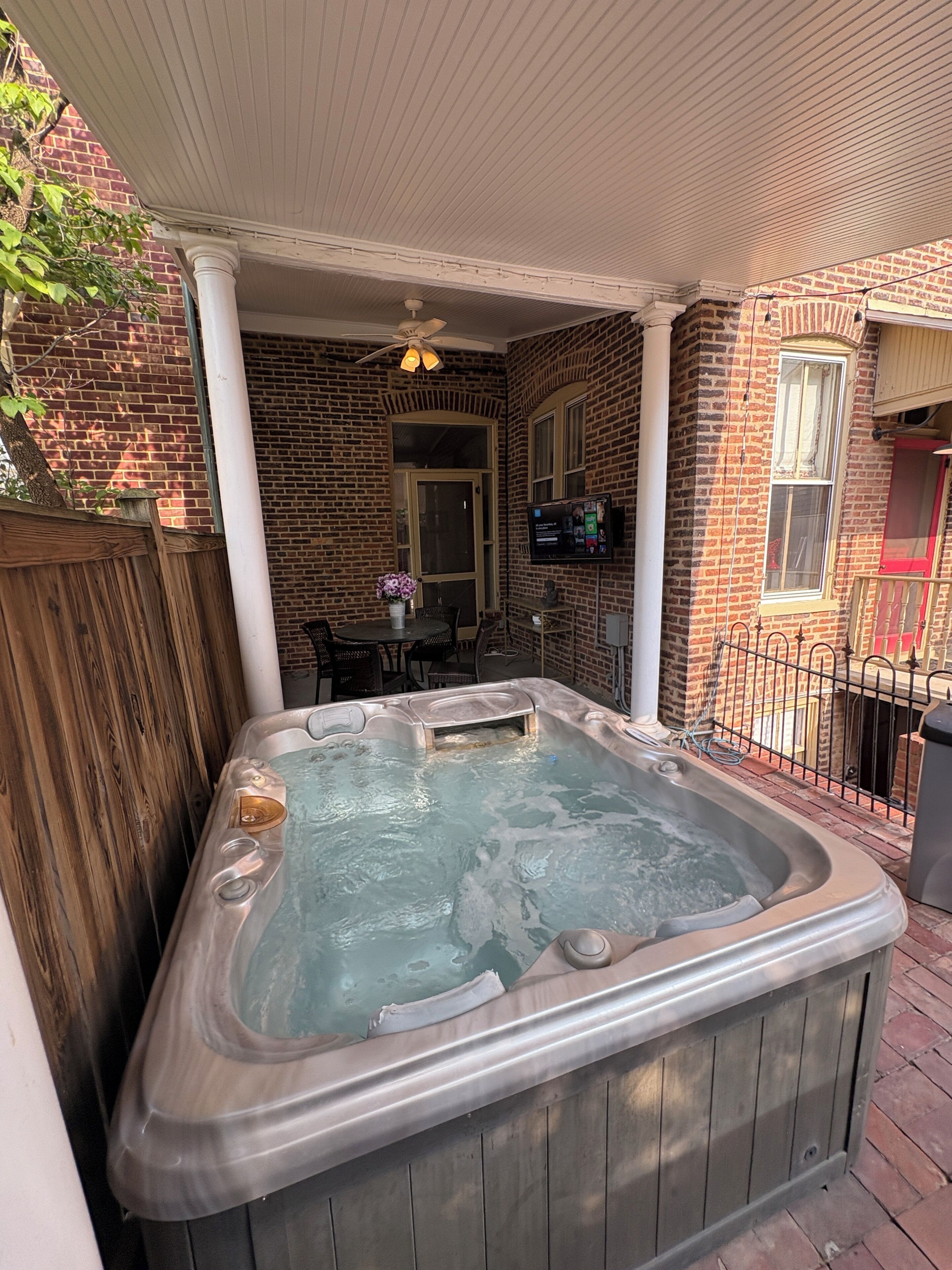 A hot tub in a covered outdoor area with brick walls and a wooden fence.