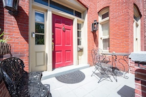 A red door with a white frame, a small outdoor table with chairs, and a metal bench. - Victorian on Washington king bed near King St Hot Tub (Alexandria)