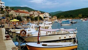 A harbor with boats docked, a small pier with a yellow umbrella, and buildings in the background. - Captivating and Spacious 2-Bed House in Vranovici (Vranovici, Kotor)