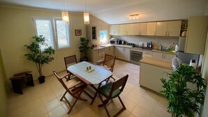 A compact kitchen with a dining table, chairs, and a microwave. There are potted plants and a bench near the window. - Captivating and Spacious 2-Bed House in Vranovici (Vranovici, Kotor)