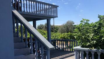 Un escalier avec des balustrades menant à une zone abritée, entourée de verdure et sous un ciel dégagé.