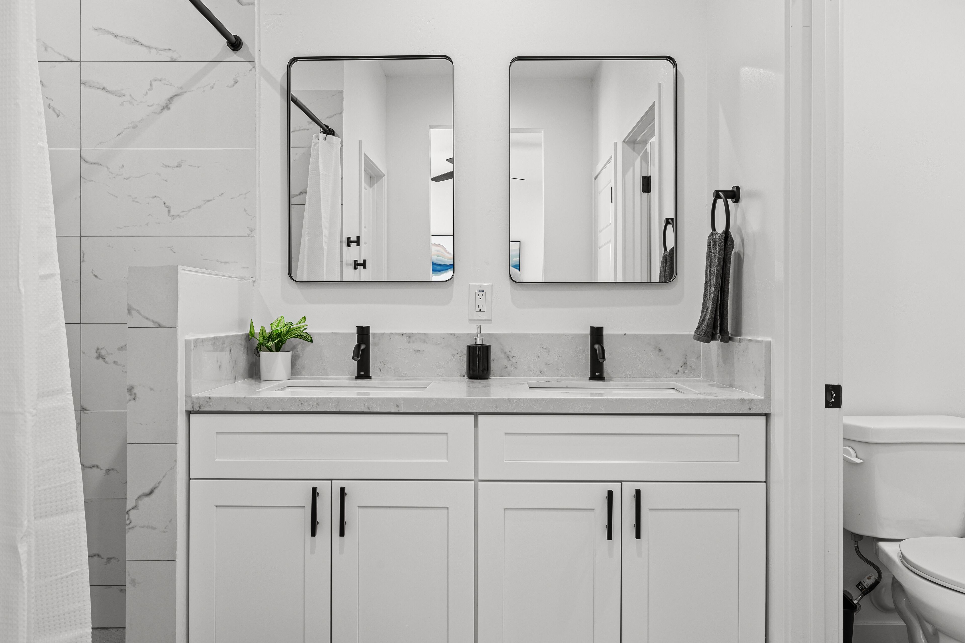 A modern bathroom with two sinks, a mirror, and a toilet.