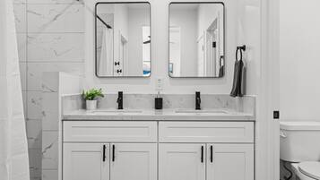A modern bathroom with two sinks, a mirror, and a toilet.