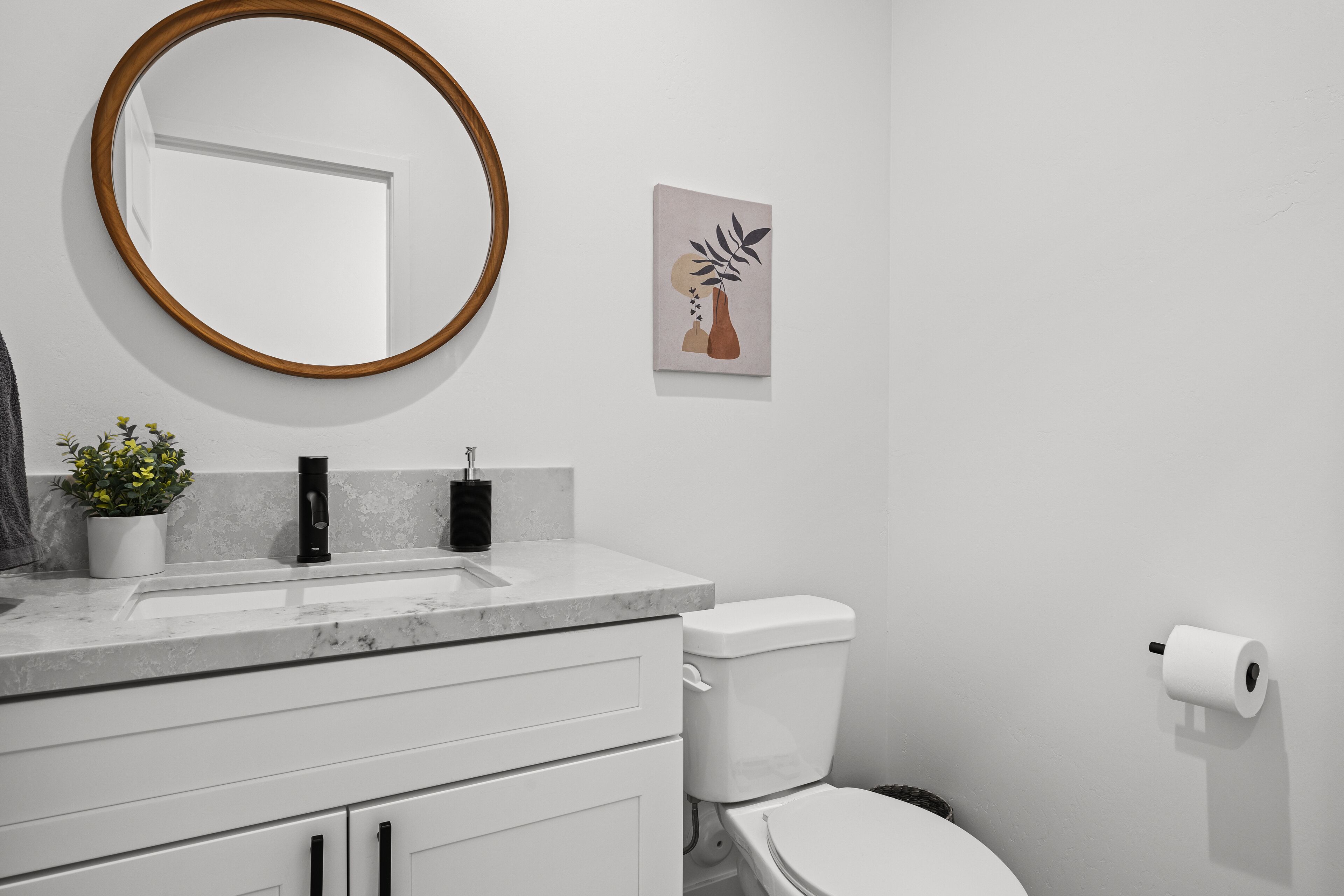 A bathroom with a white sink, a mirror with a wooden frame, a toilet, and a wall-mounted toilet paper holder.