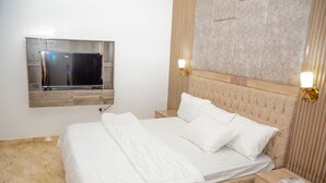 Un lit bien fait, avec du linge de lit blanc, une tête de lit en bois et une table de chevet dotée d’un tiroir.