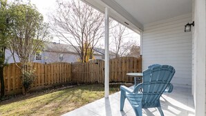 Eine überdachte Terrasse mit blauem Stuhl, kleinem Tisch, Holzzaun und einem Haus im Hintergrund.