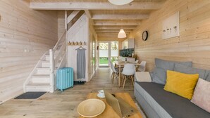 Interior acogedor de una cabaña con una escalera, un comedor, un sofá y un ordenador portátil sobre una mesa.