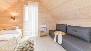 Una habitación cálida de cabaña de madera con una cama, un sofá gris, una alfombra de piel y una mesita con una lámpara.
