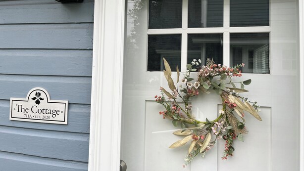 Una puerta principal con un adorno de lazo y un cartel que dice "The Cottage 711A EST. 2020".