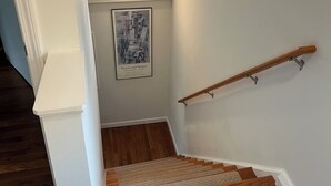 Una escalera de madera con barandilla, paredes blancas y un cartel de Picasso y Braque en la pared.