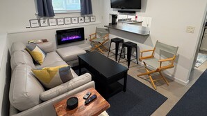 Una sala de estar con sofá, mesa de centro, televisor, chimenea y una zona de cocina.