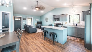 A modern kitchen with a central island, dark cabinetry, and a dining area with a wooden table and chairs. - Cozy Cabin In The Sky, with direct access to public hunting, fishing access. (Dixon)
