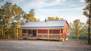 A rustic wooden cabin with a metal roof, surrounded by trees and a gravel driveway. - Cozy Cabin In The Sky, with direct access to public hunting, fishing access. (Dixon)