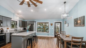 A modern kitchen with grey cabinets, a central island, and a dining area with wooden chairs. - Cozy Cabin In The Sky, with direct access to public hunting, fishing access. (Dixon)