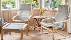 A cozy room with two chairs, a small table, and a bench. There are windows with curtains and a view of greenery outside. - "Thorke" - 200m from the sea by Interhome (Nysted)
