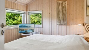 A bedroom with a bed, a television on a stand, a window with a view of greenery, and a painting on the wall. - "Thorke" - 200m from the sea by Interhome (Nysted)