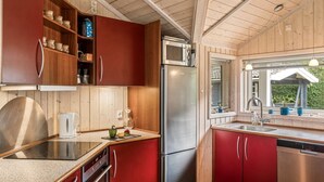 A compact kitchen with wooden cabinets, a stainless steel refrigerator, and a window with a view of greenery. - "Thorke" - 200m from the sea by Interhome (Nysted)