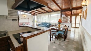 Una cocina con una isla central, vigas de madera en el techo y un comedor con sillas y una mesa.