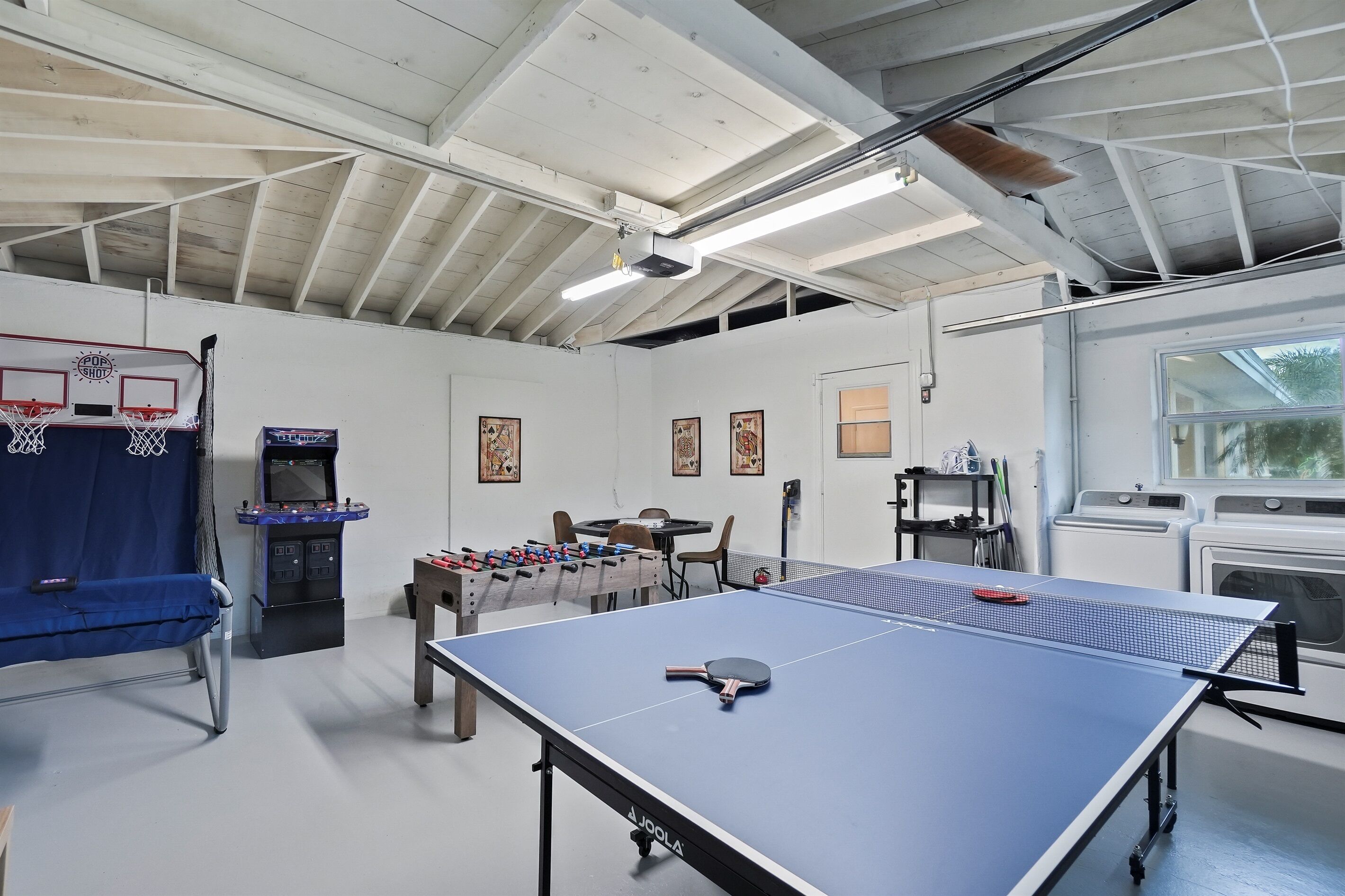 Een recreatieruimte met een tafeltennistafel, een tafelvoetbaltafel en een basketbalring.