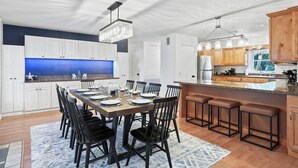 A modern kitchen with white cabinets, a blue backsplash, and a dining area with a wooden table and black chairs. - 4BR Heated Pool|12min to Beach|Gameroom|King beds (Clearwater)