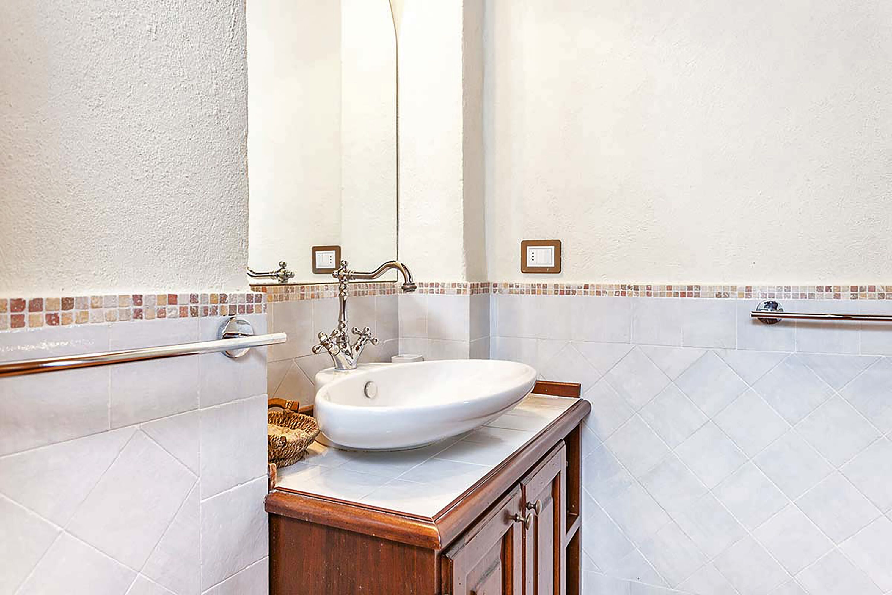 A bathroom with a white sink, wooden vanity, and a towel rack.