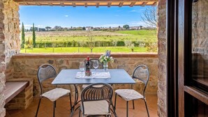 Un patio de paredes de piedra con una mesa dispuesta para dos, con vistas a un paisaje rural.