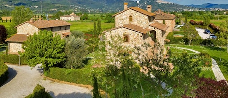 A stone building with a courtyard, surrounded by greenery and a mountainous backdrop.