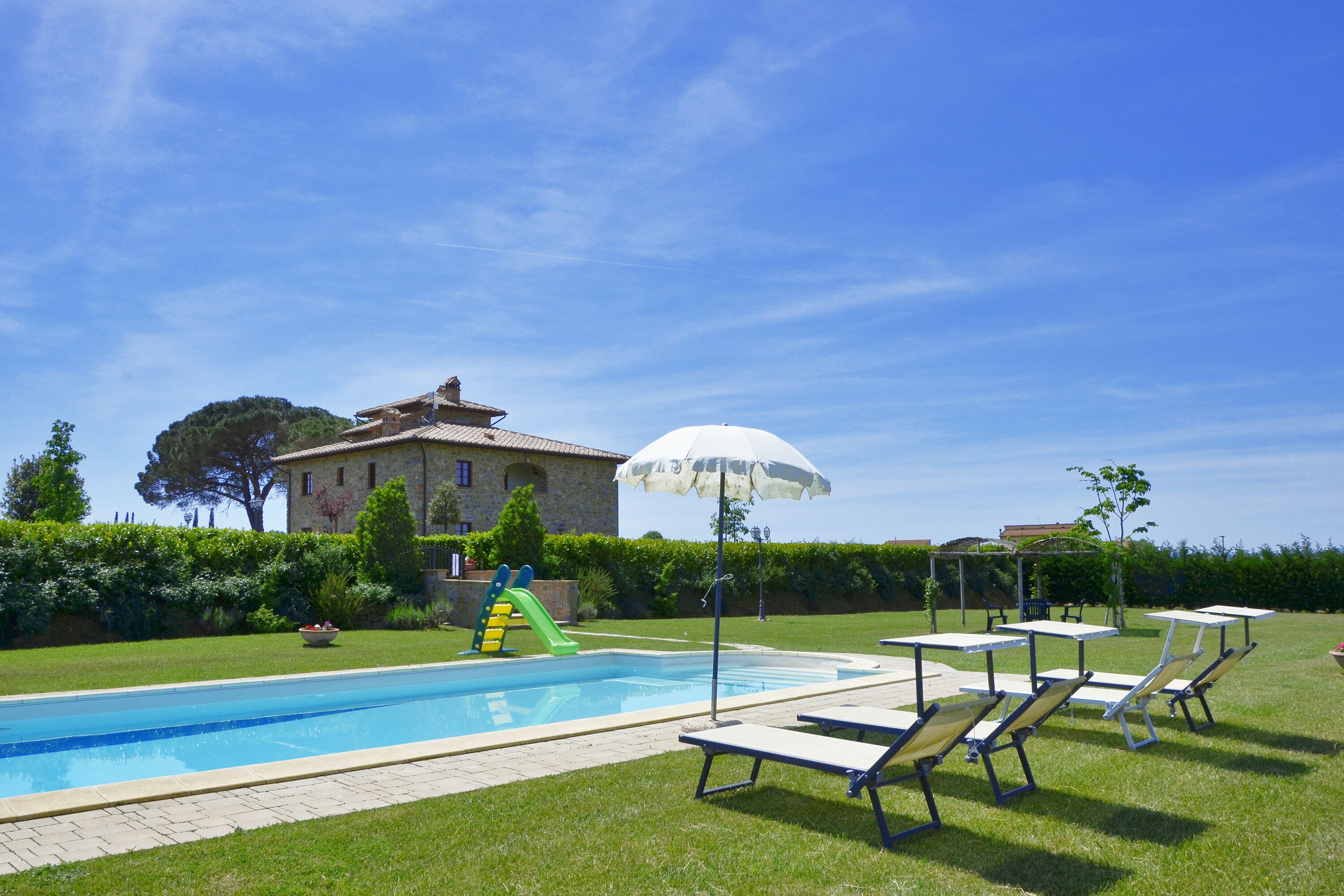 A swimming pool with lounge chairs and a slide, surrounded by a well-maintained lawn and a building in the background.