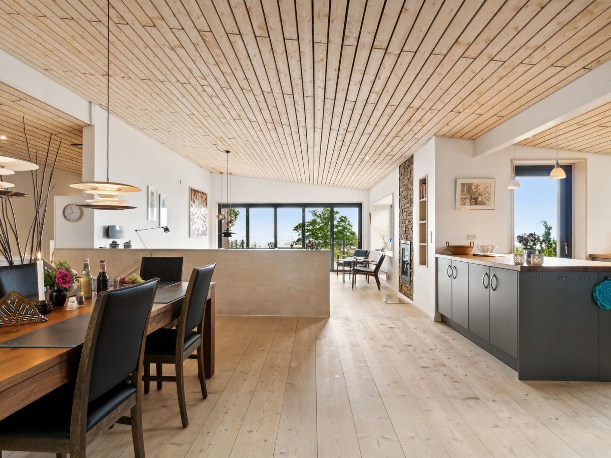 A modern kitchen with wooden flooring, a central island, and a dining area with chairs and a table.