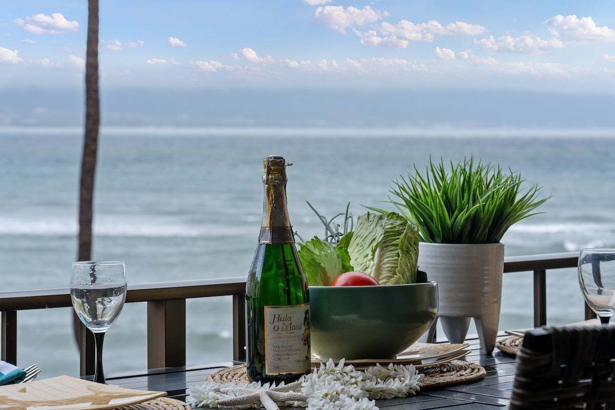 Ein Tisch mit einer Weinflasche, einer Salatschüssel und einem Glas Wasser, mit Blick auf das Meer.