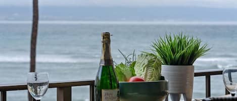 A table with a bottle of wine, a bowl of salad, and a glass of water, set against a view of the ocean.