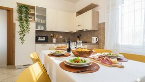 Eine moderne Küche mit weißen Schränken, einem Esszimmertisch mit angerichteten Speisen und einer hängenden Pflanze.