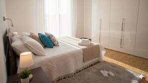 Ein Schlafzimmer mit einem Bett, einem Nachttisch, einer Lampe, einem Fenster mit durchsichtigen Vorhängen und einem Kleiderschrank.