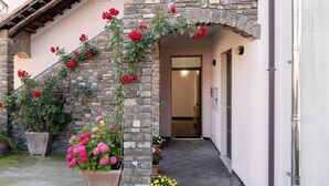 Eine Steintreppe mit roten Blumen, die zu einer Tür führt. Am Fuß befinden sich Blumentöpfe mit rosa und gelben Blüten.