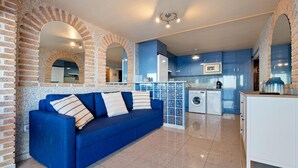 Una sala moderna con un sofá azul, una cocina con armarios azules y un área de lavandería.