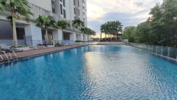 A swimming pool with lounge chairs and palm trees, surrounded by a modern building with balconies. - JB Bukit Indah Skyloft Suites (Johor Bahru)