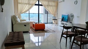 A modern living room with a sofa, ottoman, and dining area. - JB Bukit Indah Skyloft Suites (Johor Bahru)