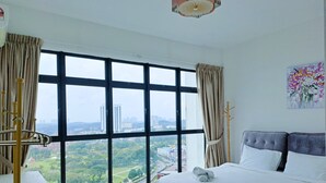 A hotel room with a large window offering a city view, a bed with white linens, and a painting on the wall. - JB Bukit Indah Skyloft Suites (Johor Bahru)