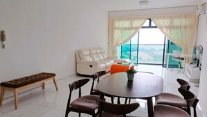 A modern living room with a round dining table, six chairs, a bench, a sofa, and a view of a green landscape through large windows. - JB Bukit Indah Skyloft Suites (Johor Bahru)
