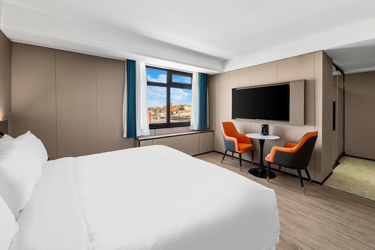 Une chambre d’hôtel avec un grand lit, un téléviseur fixé au mur, deux fauteuils et une fenêtre donnant sur la ville.