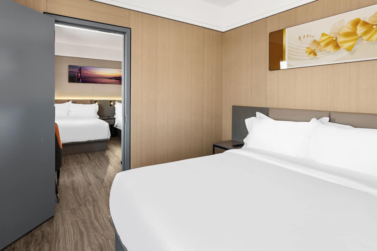 Une chambre d’hôtel avec un grand lit, une table de chevet, une commode et une porte donnant sur une autre pièce.