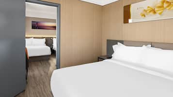 A hotel room with a large bed, a bedside table, a nightstand, and a door leading to another room.