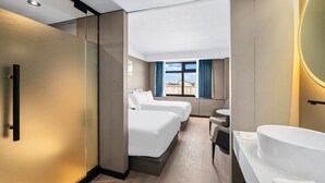 Een hotelkamer met een bed, bureau, stoel, badkamer met wastafel en raam met gordijnen.