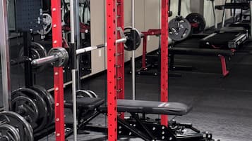 A gym with a red and black weightlifting station, a bench, and various weights.