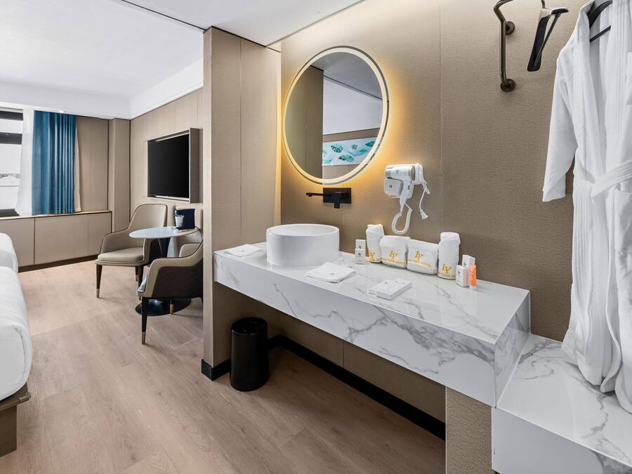 Una moderna camera d'hotel con una toeletta in marmo, uno specchio tondo con illuminazione integrata, un asciugacapelli e un accappatoio appeso al muro.