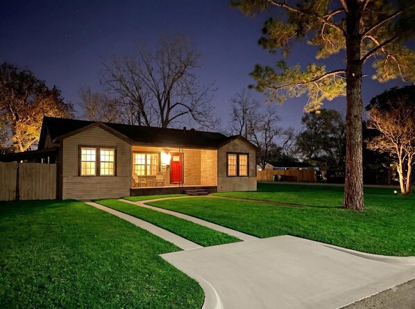 A two-story house with a front porch, a red door, and a well-maintained lawn.